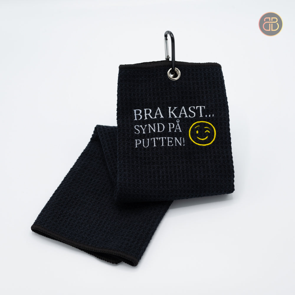 Disc golf towel with the text Bra kast synd på putten and a smiley in yellow