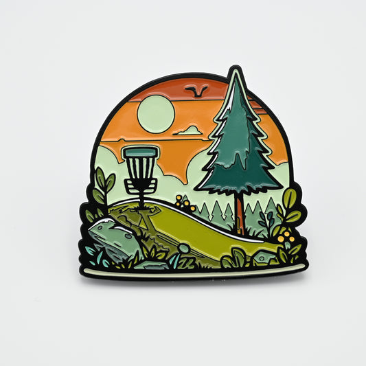 Discgolf pin with a discgolf basket standing on a mountain with trees in the background. A sunset in the background aswell.