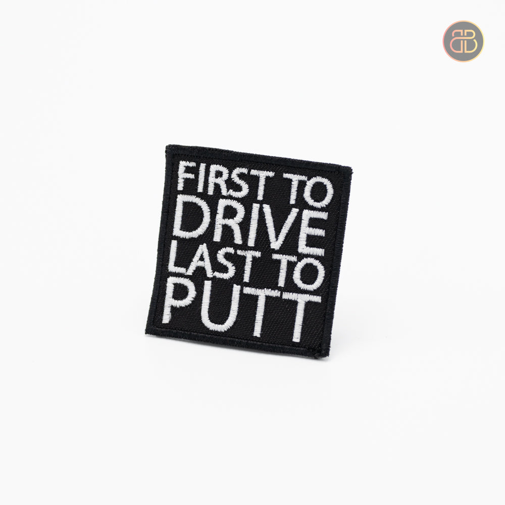 Discgolf patch in black with the text First to drive last to putt in white