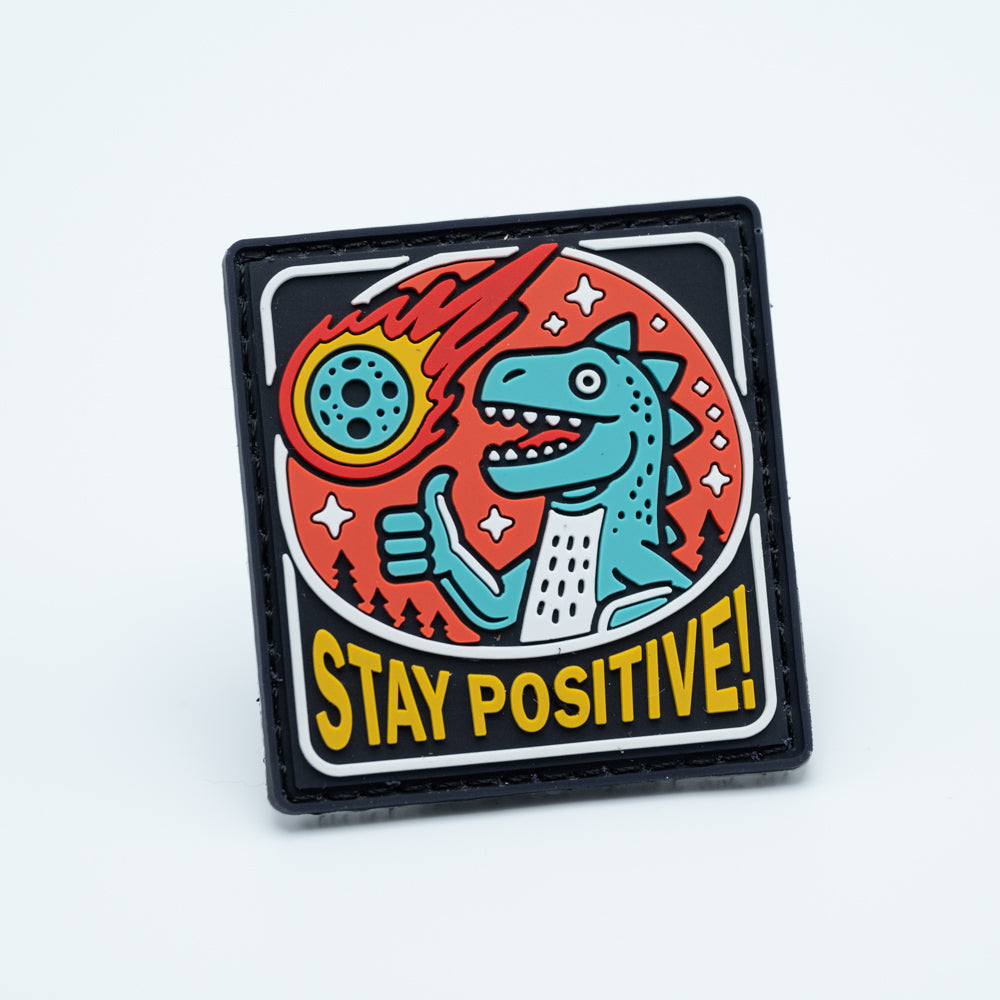 Discgolf patch in pvc with a meteor crashing in the earth and a dinasour holding a thumbs up with the text Stay positive!
