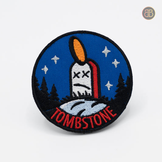 Discgolf patch with a discgolf disc being stuck to a tombstone. The text TOMBSTONE is in the bottom of the discgolf patch