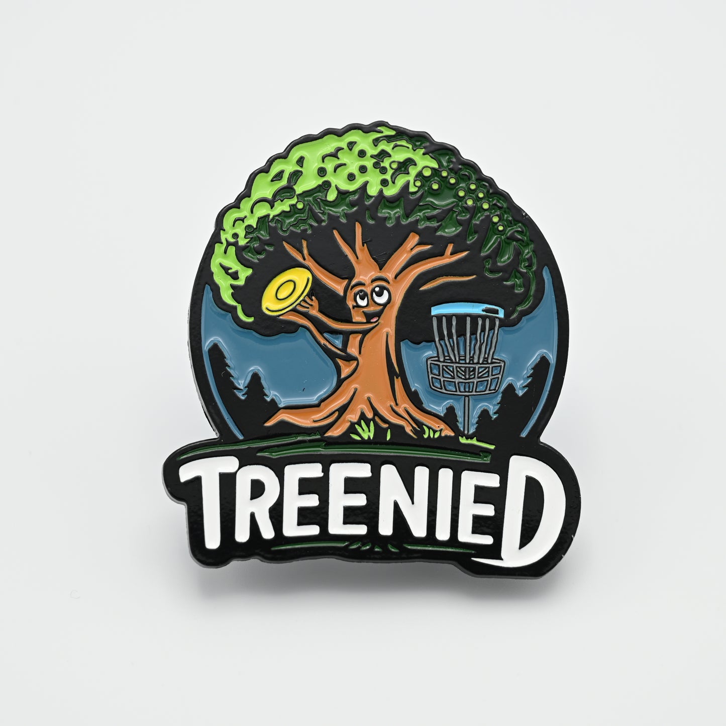 Discgolf pin with a tree grabbing a discgolf disc that is on the way into the discgolf basket, with the text TREENIED underneath