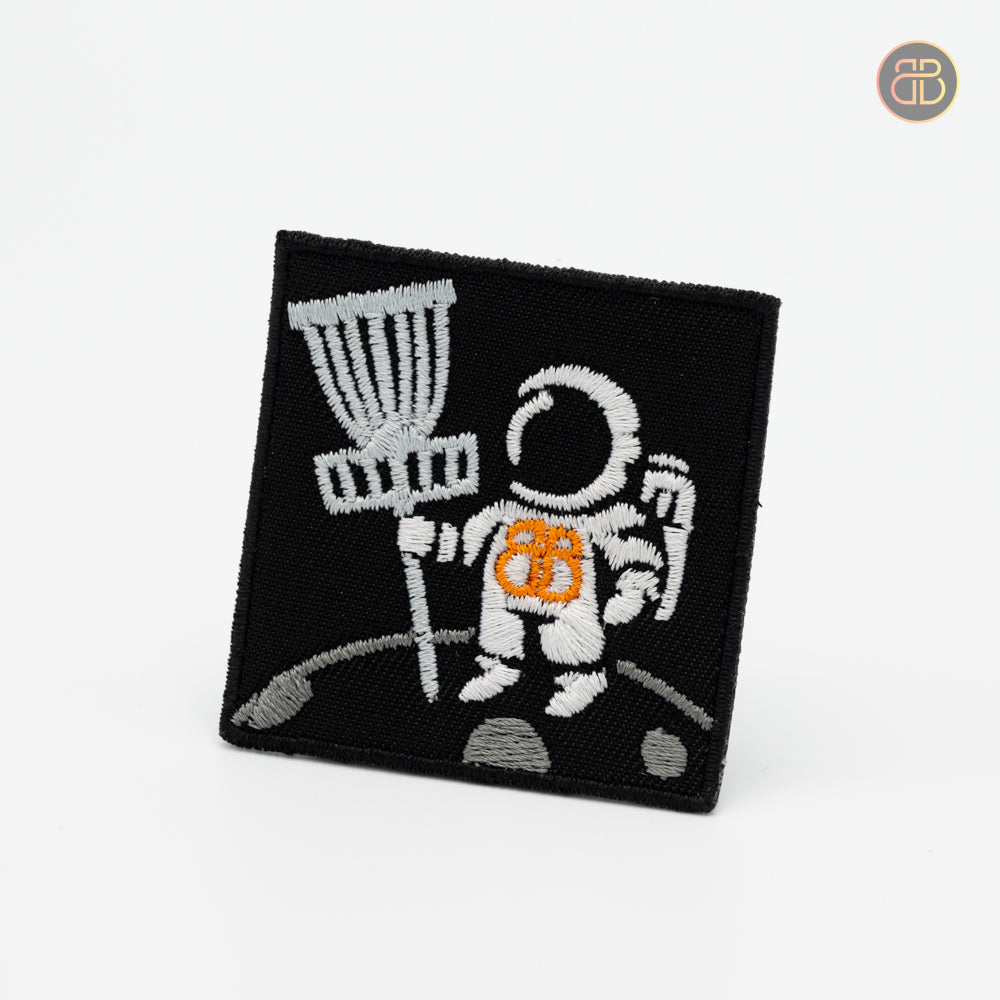 Discgolf patch showing the first human on the moon with a discgolf basket