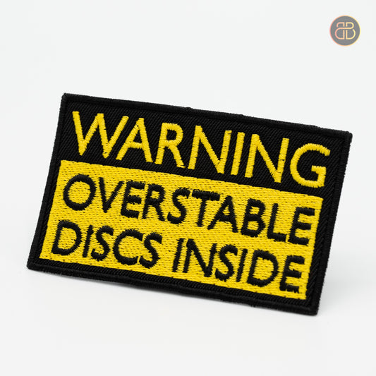 Discgolf patch with the text WARNING OVERSTABLE DISCS INSIDE