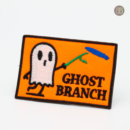 Discgolf patch with the text Ghost Branch and a cartoon poiting a stick to a discgolf disc